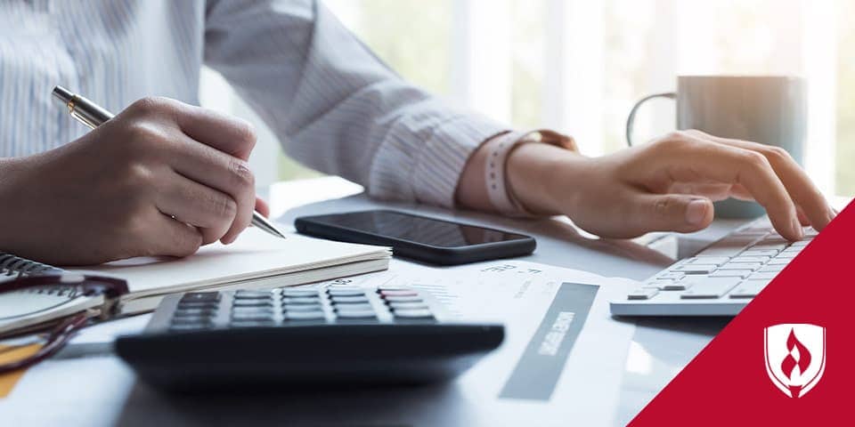 person at desk with one had on keyboard and one hand writing