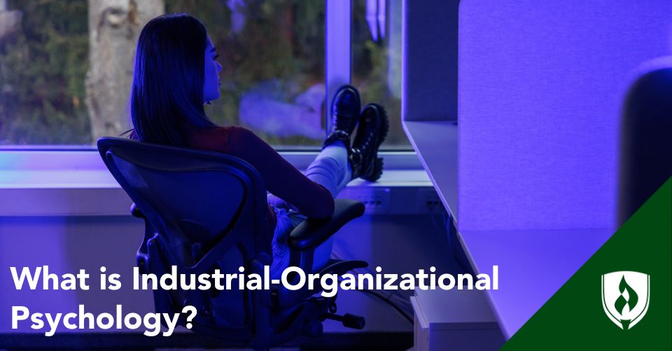 A business professional sits at a desk in purple light