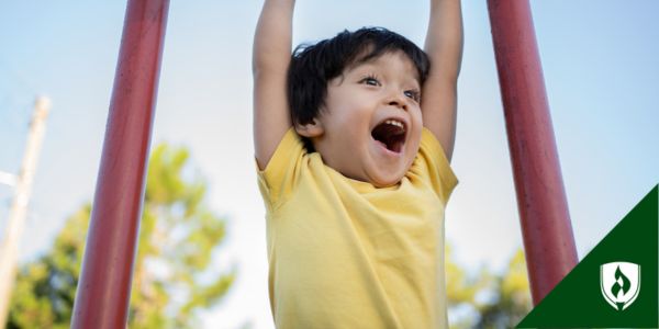 A young child swings on the monkey bars with a delighted expression on his face