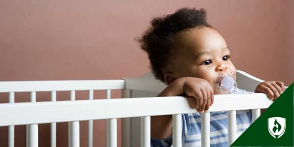A very adorable toddler holds onto the side of their crib