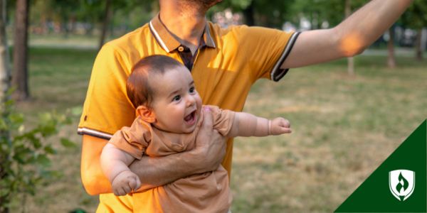 A parent in a yellow shirt plays with his infant in the park