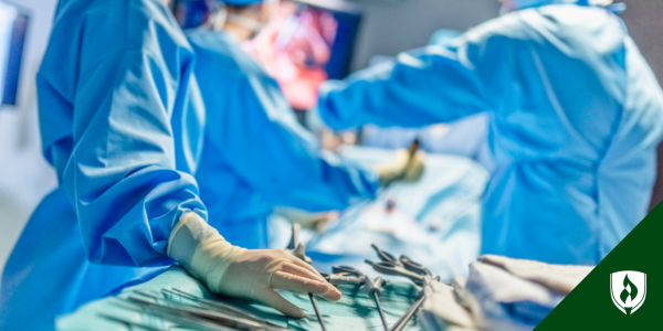 A close up view of a surgical tech in full scrub, reaching for a surgical tool