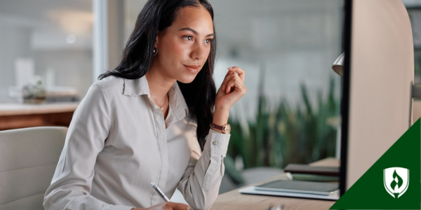 A medical coder jots a note while looking at her computer screen in an office