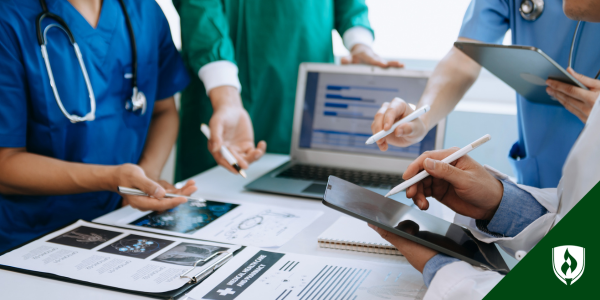 A nurse meets with a healthcare team over a table strewn with documents