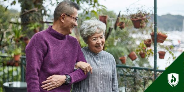 An elderly couple walk arm in arm through a garden