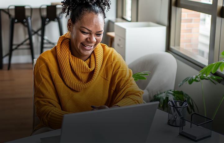 Woman in yellow sweater smiling in front of laptop